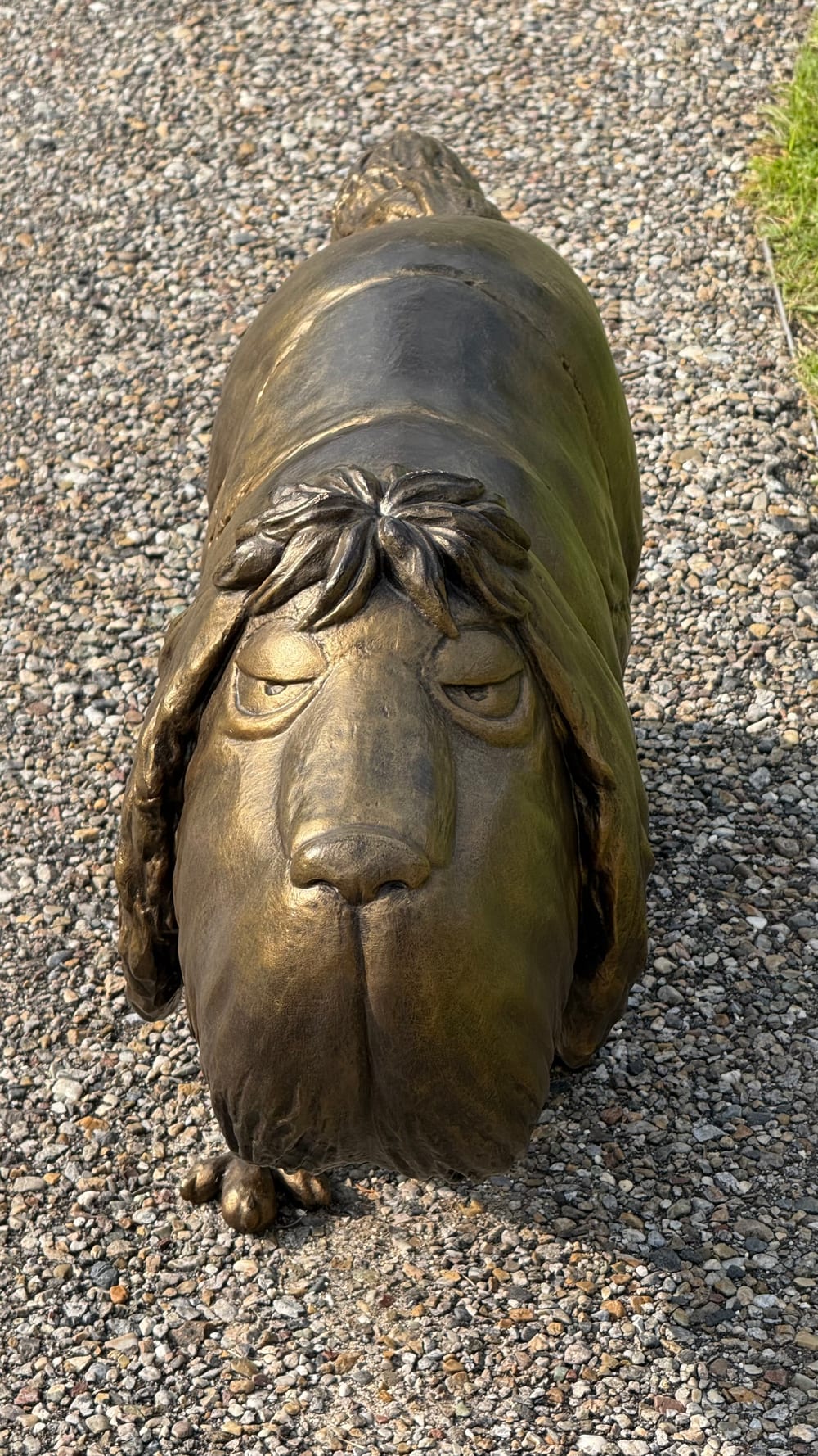 A bronze statue of a dog standing on gravel, seen from the front
