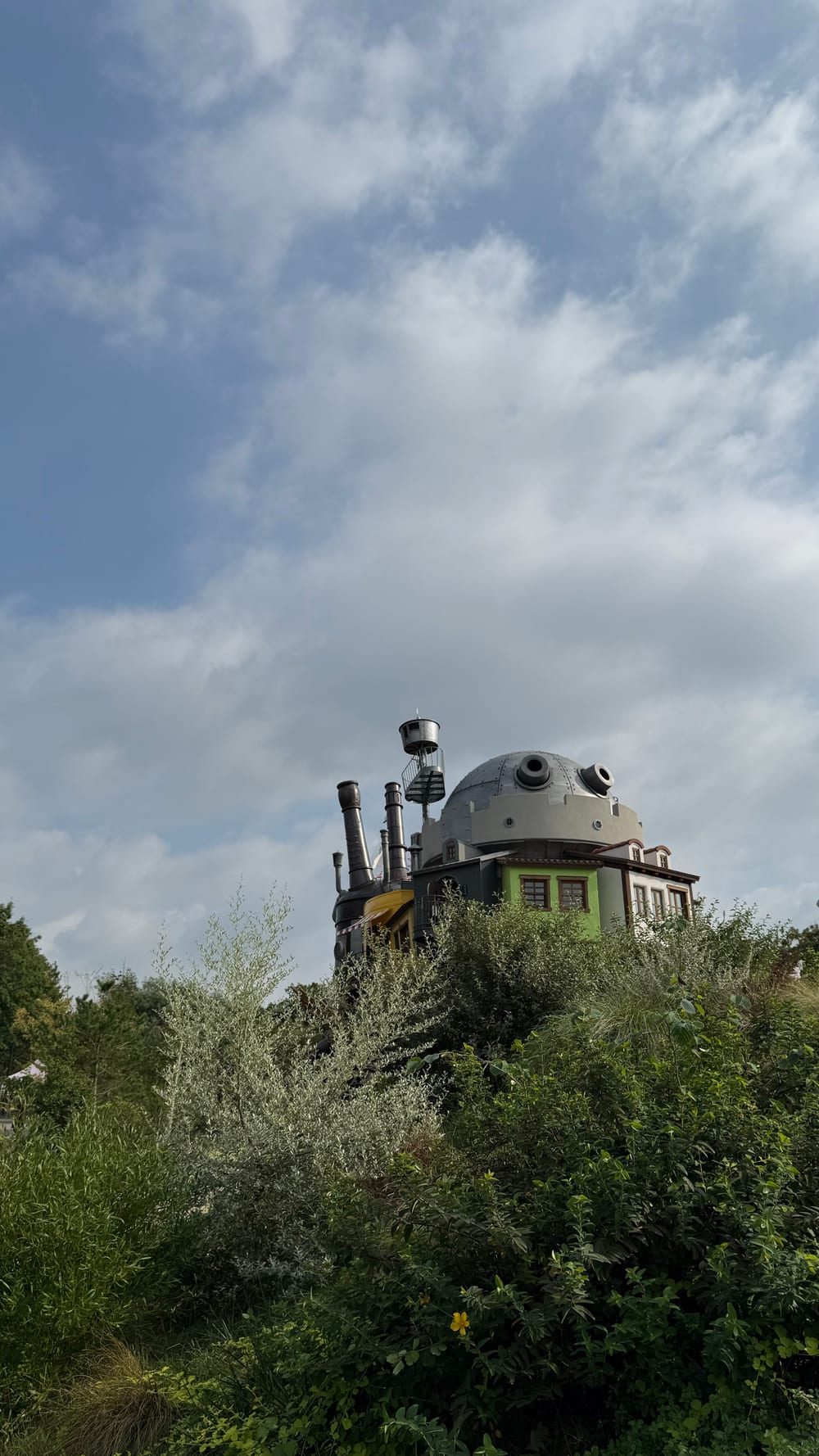 Howl’s castle seen from below over scrub, the dome and chimneys above the bushes